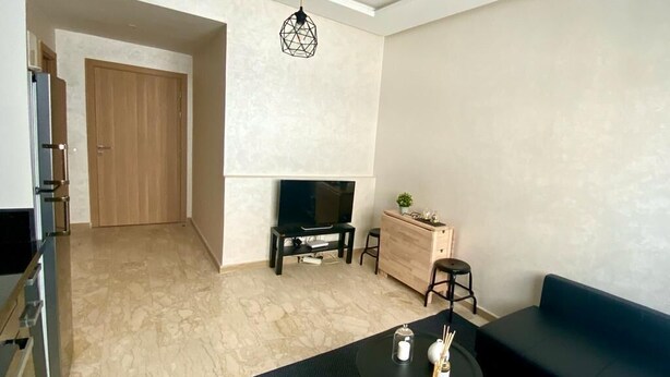 A modern living room with a sofa, a small round table, a TV, and a wooden cabinet. - Appartement Lumineux et Confortable Près de Novotel Face au Parc (Mohammedia)