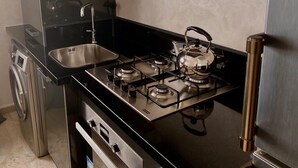 A compact kitchen with a gas stove, a sink, and a stainless steel range hood. - Appartement Lumineux et Confortable Près de Novotel Face au Parc (Mohammedia)