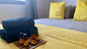 A bed with a yellow blanket, a blue towel, and several bottles on a wooden tray. - Appartement Lumineux et Confortable Près de Novotel Face au Parc (Mohammedia)