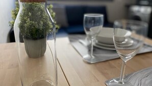 A dining table with a clear glass vase containing green plants, a wine glass, and a plate. - Appartement Lumineux et Confortable Près de Novotel Face au Parc (Mohammedia)