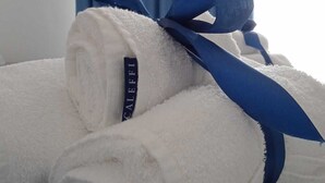 Two rolled white towels with a blue ribbon tied around them, placed on a patterned fabric. - Aquamarine apartment (Avola)