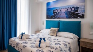 A hotel room with a bed, a painting of a pier, and a window with blue curtains. - Aquamarine apartment (Avola)