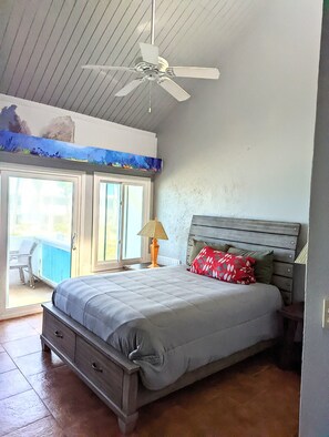 Une chambre à coucher avec un lit, un ventilateur de plafond, une fenêtre et une vue sur l’extérieur.