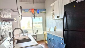 Cozinha com geladeira preta, armários azuis e janela com vista para edifícios.