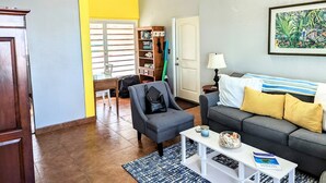 Uma sala de estar com um sofá cinzento, uma pequena mesa de centro branca e uma estante de livros.