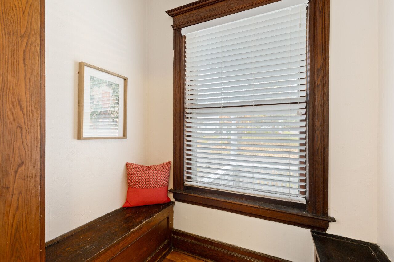 Ein Zimmer mit einer hölzernen Sitzbank, einem gerahmten Bild an der Wand und einem Fenster mit Jalousien.