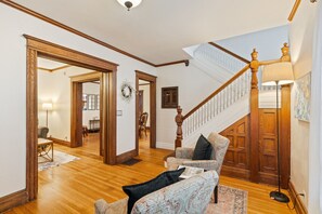 A spacious living room with a wooden staircase, a patterned sofa, and a lamp. - Spacious 4 BDRM w/Onsite Parking & A/C! (Rochester)
