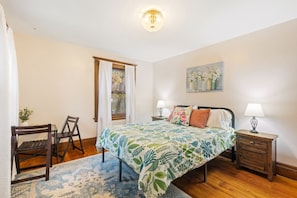 A bedroom with a bed, nightstands, a chair, a window with curtains, and a painting on the wall. - Spacious 4 BDRM w/Onsite Parking & A/C! (Rochester)