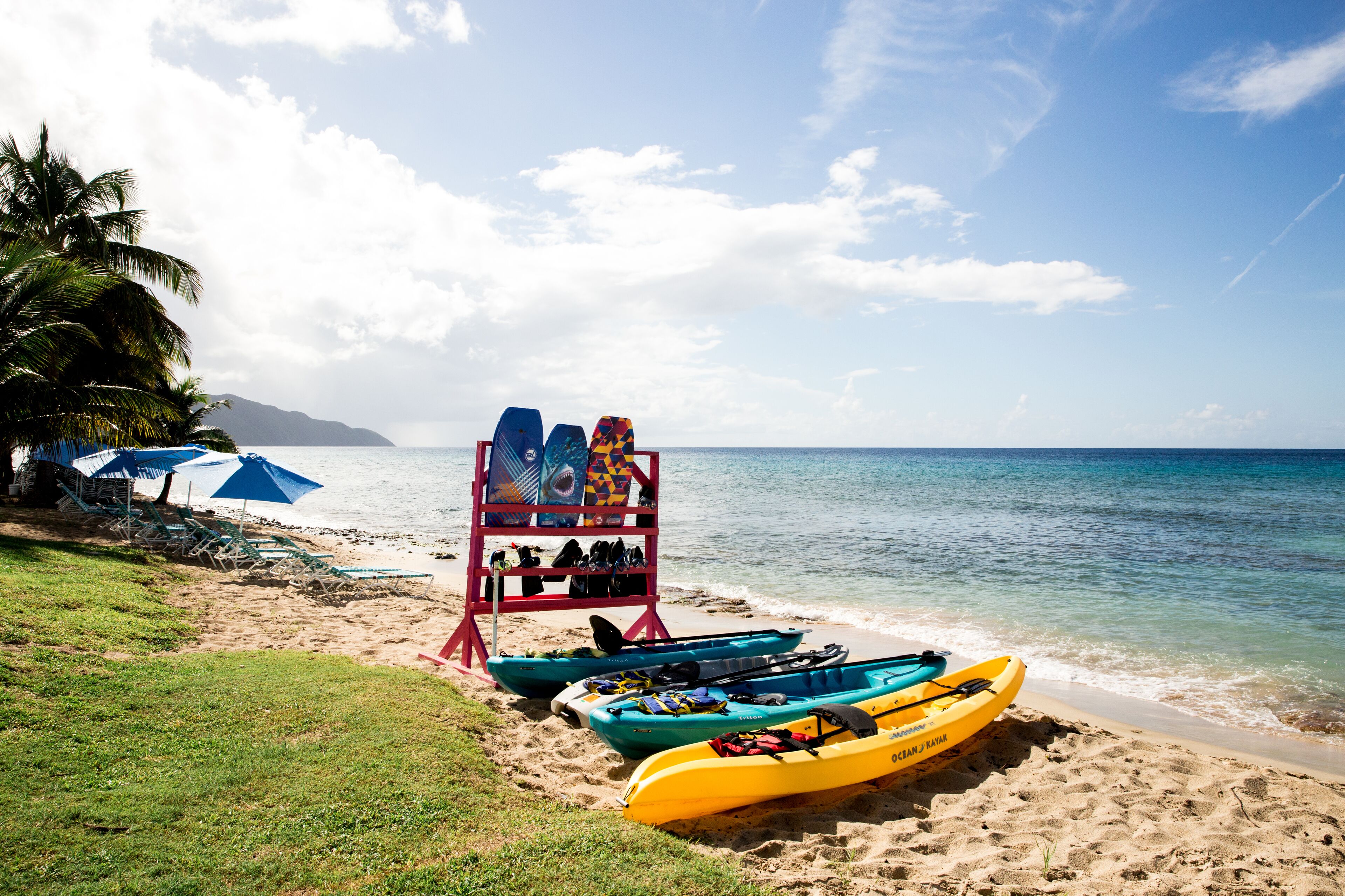Una playa con kayaks, un puesto de salvavidas y sombrillas.