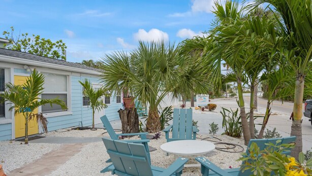A patio area with outdoor seating, palm trees, and a building with a yellow door. - Flamingo 1BR Beach-side Villa in Siesta Key - Pool (Siesta Key)