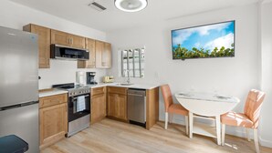 A modern kitchen with wooden cabinets, stainless steel appliances, a dining area with a white table and peach chairs, and a ceiling light fixture. - Flamingo 1BR Beach-side Villa in Siesta Key - Pool (Siesta Key)