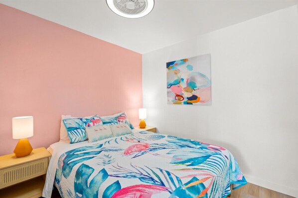 A bedroom with a pink wall, a bed with a floral bedspread, two bedside lamps, and a ceiling fan.
