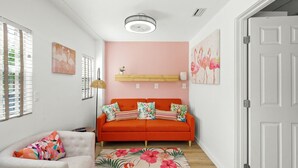 A room with a red sofa, a white armchair, a wooden shelf, and a pink wall. - Flamingo 1BR Beach-side Villa in Siesta Key - Pool (Siesta Key)