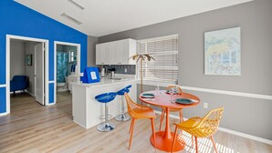 Une cuisine moderne avec des meubles blancs, un îlot central et un coin repas agrémenté de chaises orange et d’une table rouge.