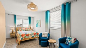 Ein Schlafzimmer mit einem Bett, zwei blauen Sesseln, einem kleinen runden Tisch und einer Pendelleuchte.