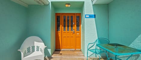 A turquoise building with a wooden deck, a wooden door with a sign reading "GULF", and a table with chairs.