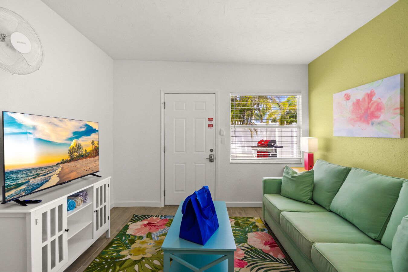 A living room with a television, a green sofa, a blue table, and a floral rug.