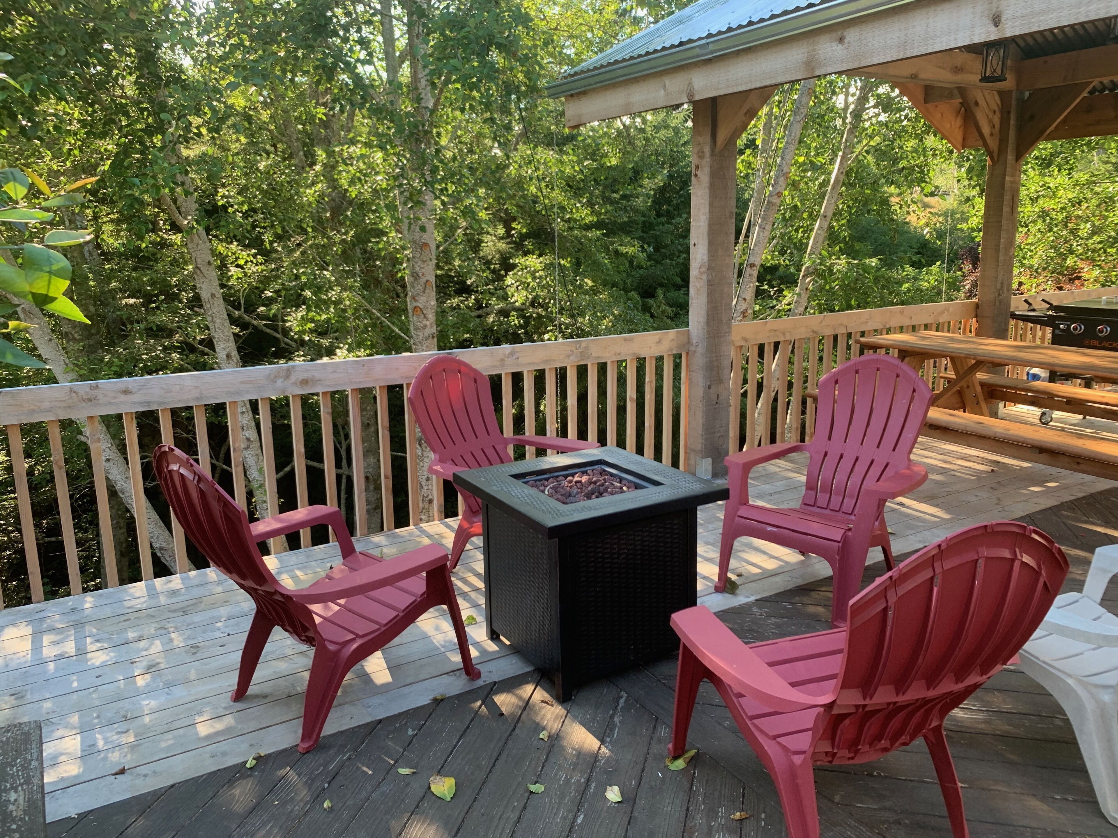 A deck with a fire pit table and four Adirondack chairs.
