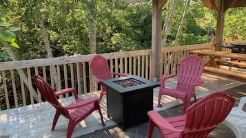 A deck with a fire pit table and four Adirondack chairs.