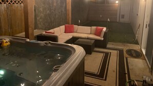 A cozy outdoor seating area with a hot tub, a cushioned sofa with red cushions, and a wooden pergola with string lights. - Macklyn Creek retreat (Brookings)