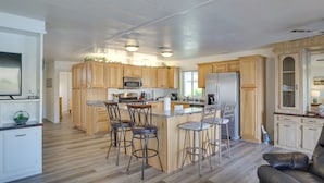 Una cocina amplia con armarios de madera, una isla central con taburetes de bar y un refrigerador.