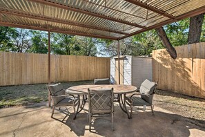 A covered patio with a round table and four chairs, surrounded by a wooden fence and a small shed. - 1 Mi to UTA: Arlington Elm Cottage w/ Fenced Yard (Arlington)