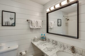 Un baño con un espejo grande, azulejos blancos, encimera de mármol, un lavabo y un perchero para toallas.