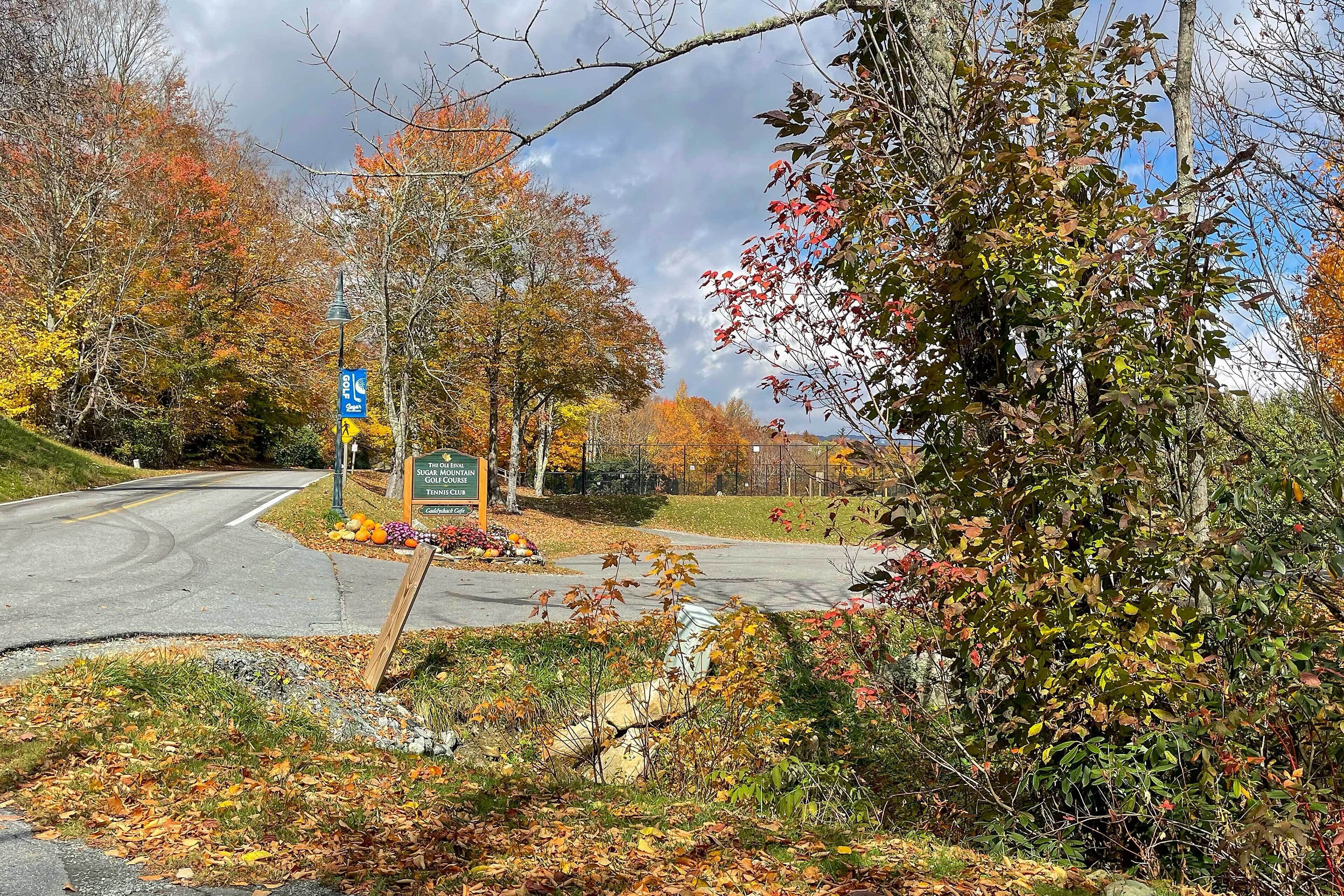 A golf course entrance with a sign, trees in autumn colors, and a road.