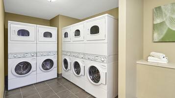 A laundry room with four stacked washers and dryers, a tiled floor, and a wall-mounted towel rack.