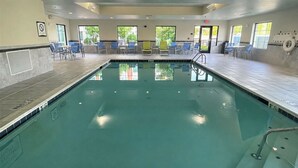 Une piscine intérieure à l’eau claire, entourée de chaises et de tables bleues, et dotée de grandes fenêtres laissant entrer la lumière naturelle.