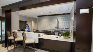 Un espace d’accueil d’hôtel au design moderne, comprenant un comptoir d’accueil, un coin salon et une grande fresque murale représentant un pont.