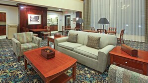 Un hall d’hôtel avec un tapis à motifs, un canapé, des fauteuils, une table basse en bois et un coin repas avec des chaises et une table.