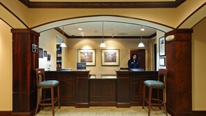 Un espace d’accueil comprenant un comptoir en bois, deux tabourets de bar et une réceptionniste.