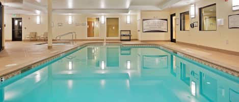 A large indoor swimming pool with clear water, surrounded by beige walls and a tiled floor.