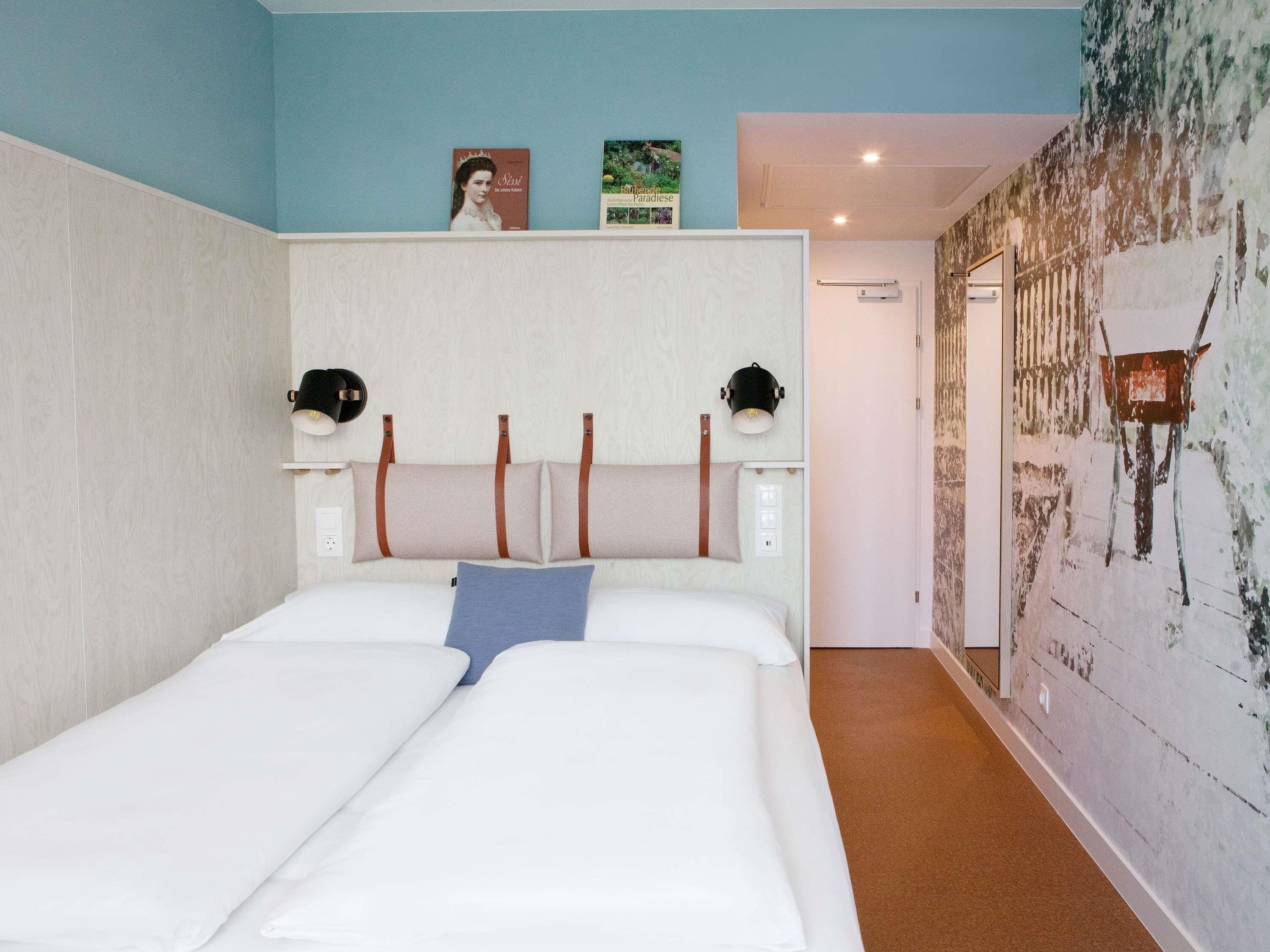 Ein Schlafzimmer mit einem Bett, zwei Wandlampen, einem Kopfteil und einer Wand mit einem Gemälde.