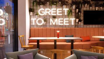 Ein moderner Lounge-Bereich mit einer Couch und Sesseln, einer Neon-Schriftzugtafel mit der Aufschrift "GREET TO MEET" und Topfpflanzen an der Wand.
