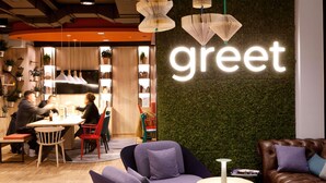 A modern interior with a 'greet' sign, seating areas, and a bookshelf with books and plants. - Greet Wien City Nord  (Vienna)