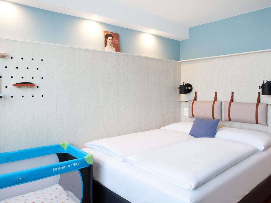 Una habitación de hotel con una cama, una cuna y un aplique de pared.