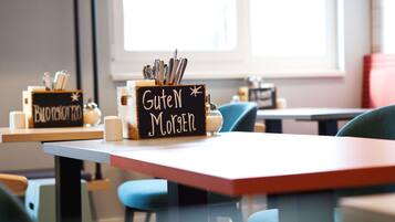 Une table préparée pour le petit-déjeuner, avec une pancarte indiquant « Guten Morgen » et un récipient contenant des couverts.