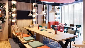 A modern library with wooden bookshelves, a long table with colorful chairs, and pendant lighting. - Greet Wien City Nord  (Vienna)