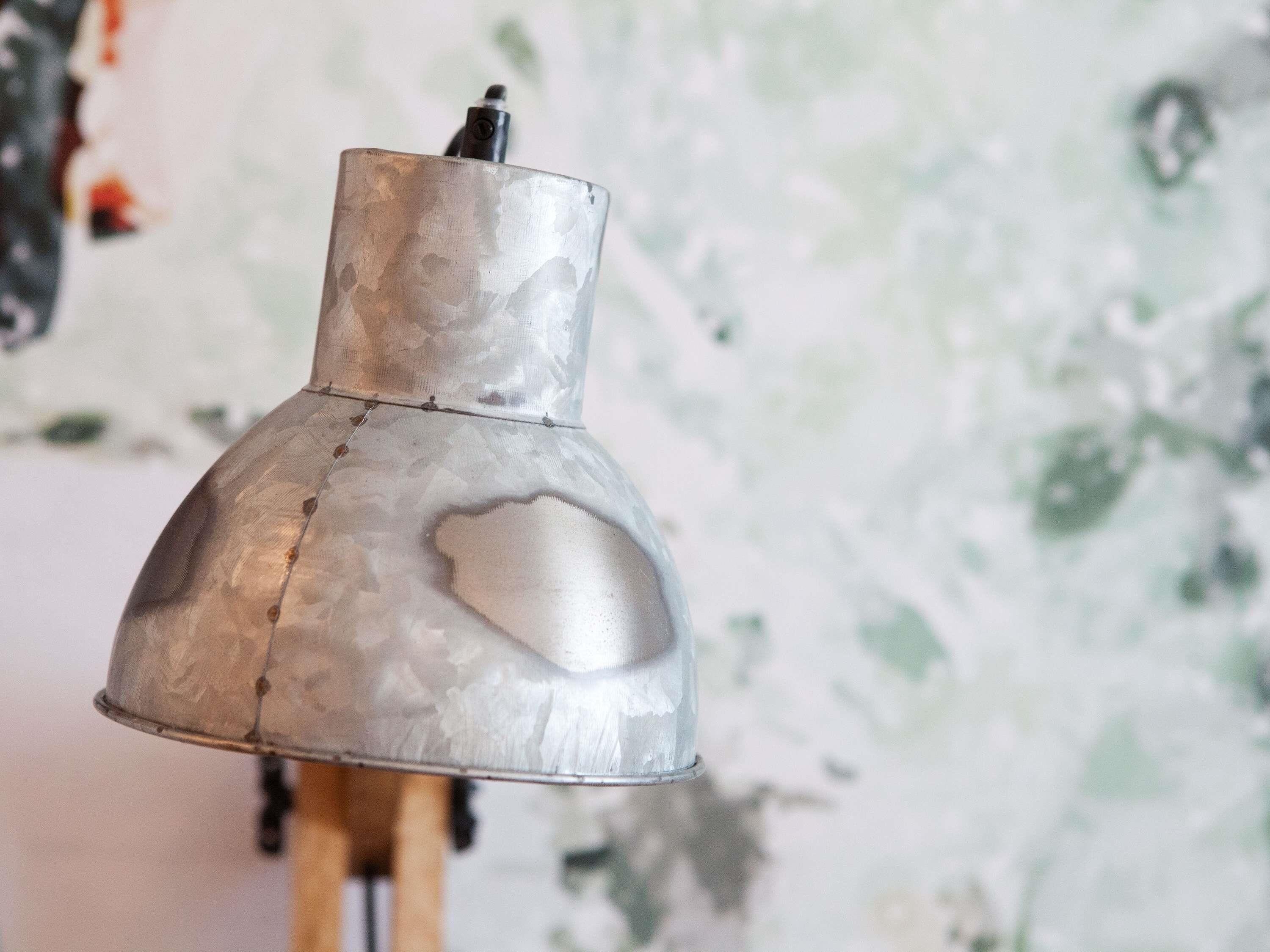 Un oggetto metallico a forma conica con un elemento sporgente sulla parte superiore, probabilmente un lampadario, su una parete strutturata.