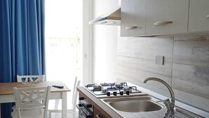 Une cuisine de taille réduite, équipée d’une cuisinière à gaz, de deux éviers et de meubles de rangement en bois.