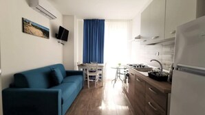 Un espace de vie compact comprenant un canapé, une table à manger, des chaises, un coin cuisine avec une cuisinière et un évier, ainsi qu’un téléviseur à écran plat fixé au mur.