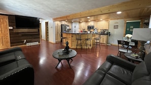 A spacious living room with a large TV, a wooden floor, and a kitchen area with wooden cabinets and a bar. - Cozy Cottage (Roscommon)