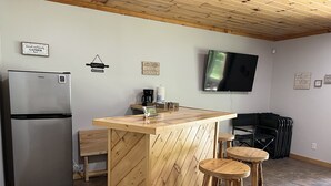 A compact kitchen with a Galanz refrigerator, wooden bar counter, stools, and a flat-screen TV mounted on the wall. - Cozy Cottage (Roscommon)