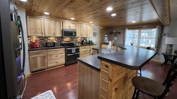 A modern kitchen with wooden cabinets, a stainless steel refrigerator, a microwave, and a large island with bar stools. - Cozy Cottage (Roscommon)