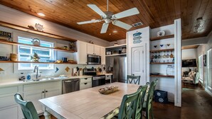 Una cucina con mobili bianchi, soffitto in legno e zona pranzo con sedie verdi.