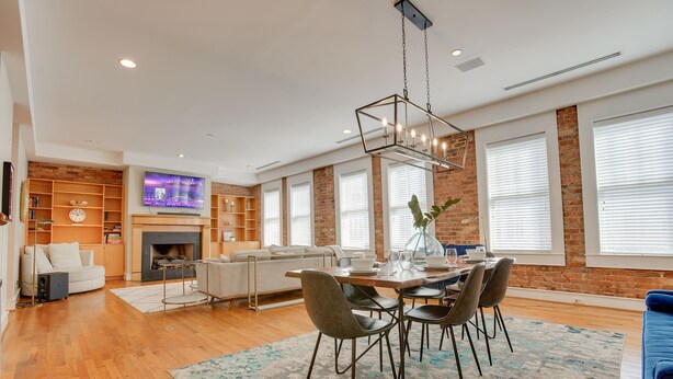 Un salon moderne avec une cheminée, un coin repas agrémenté d’un lustre et un téléviseur fixé au mur.