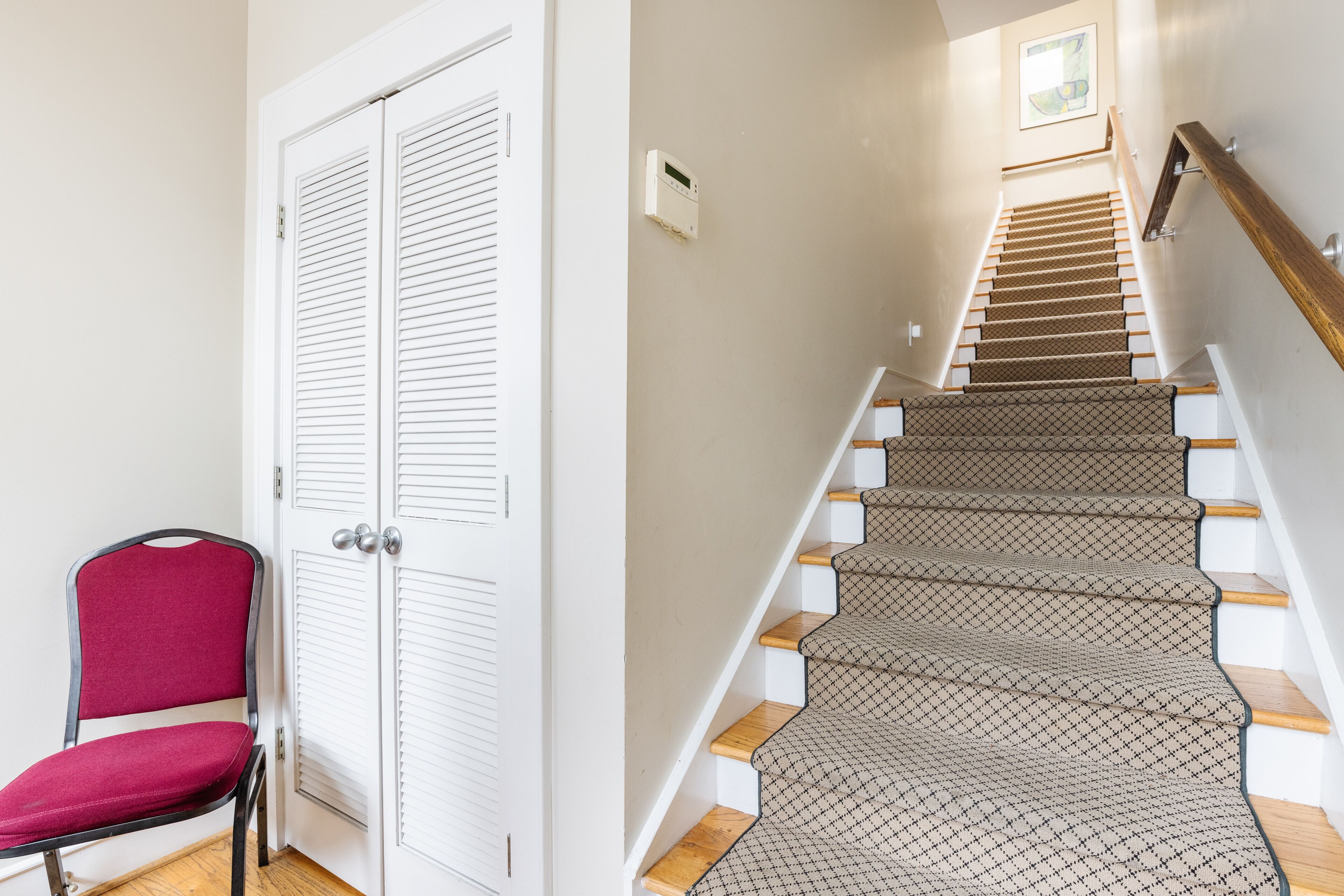 Un escalier recouvert d’une moquette à motifs et doté de marches en bois, une chaise rouge et une porte blanche à panneaux ajourés.