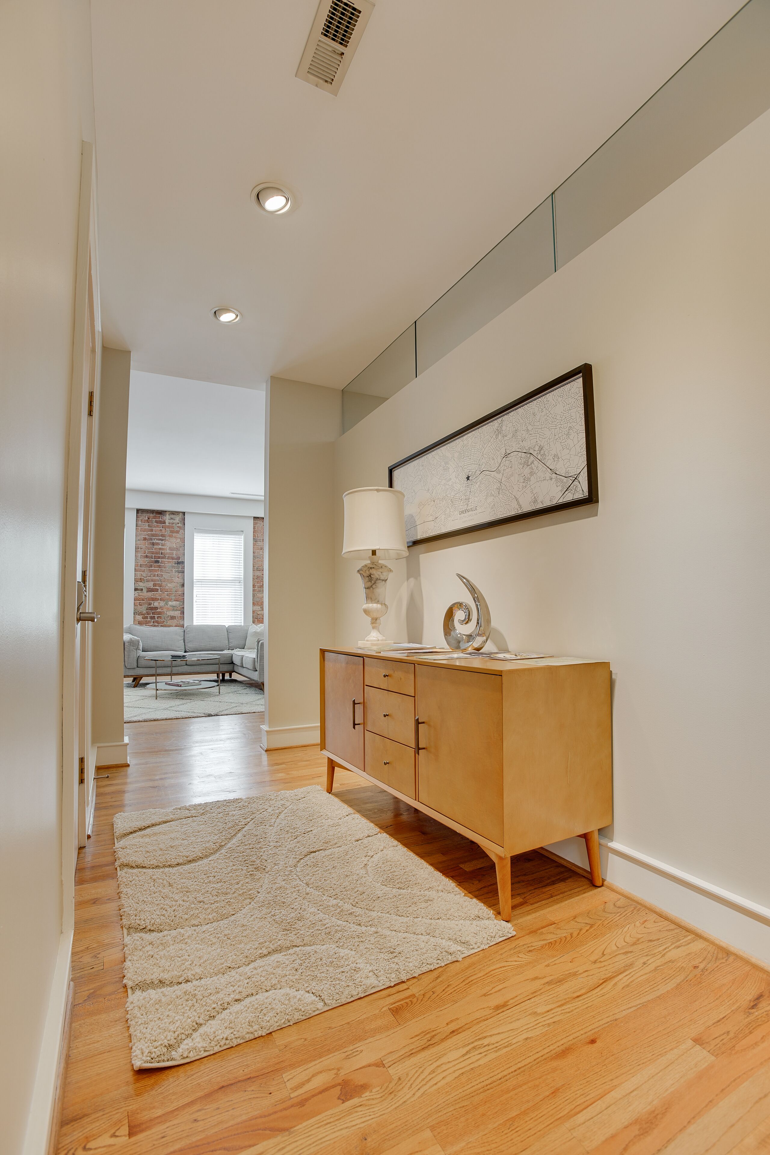 A hallway with a wooden floor, a beige rug, a wooden cabinet, and a framed map on the wall.